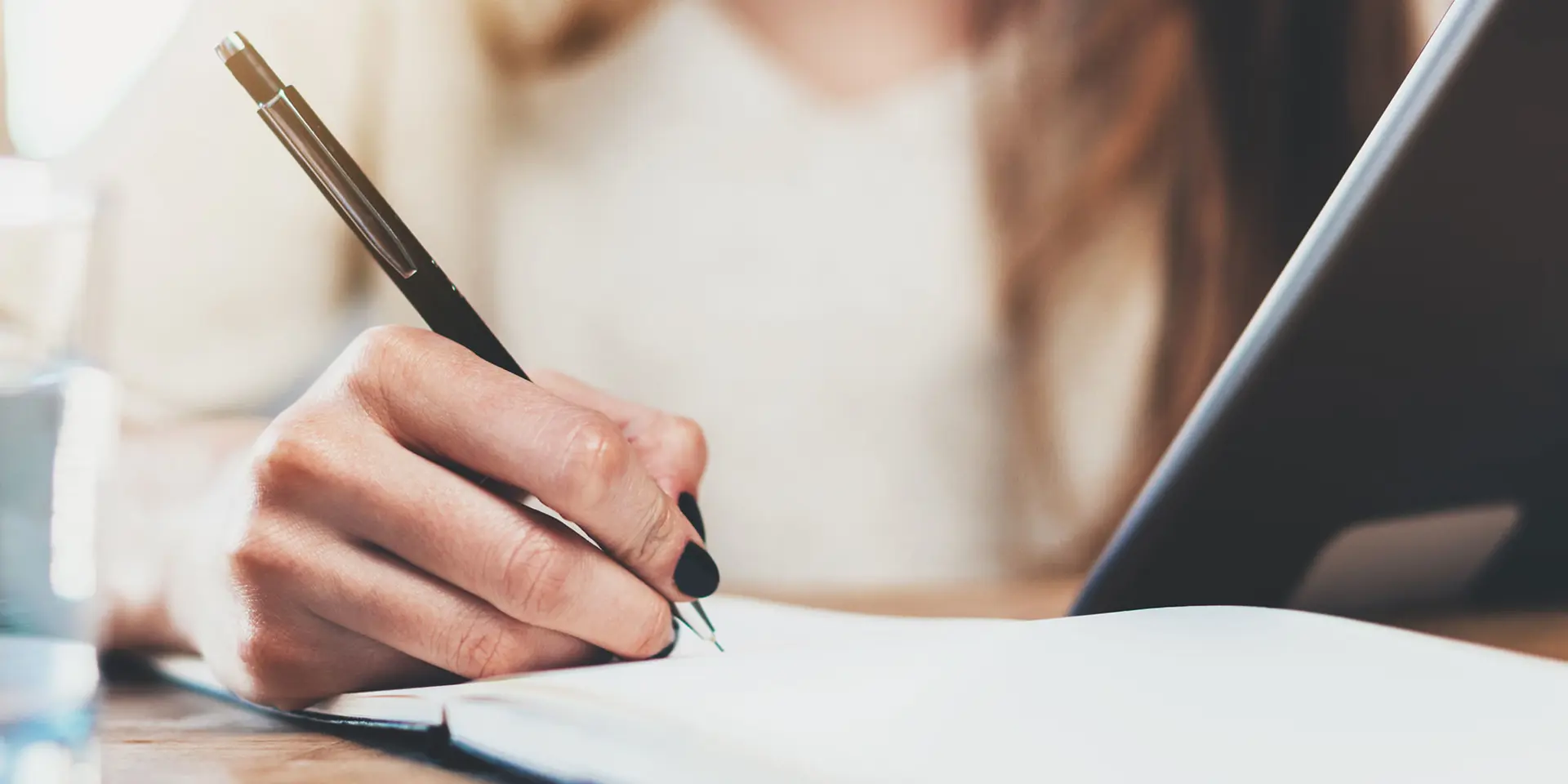 Kvinde med løst hår og sort neglelak skriver i sin notesbog. Med sin venstre hånd holder hun på et dokument. 